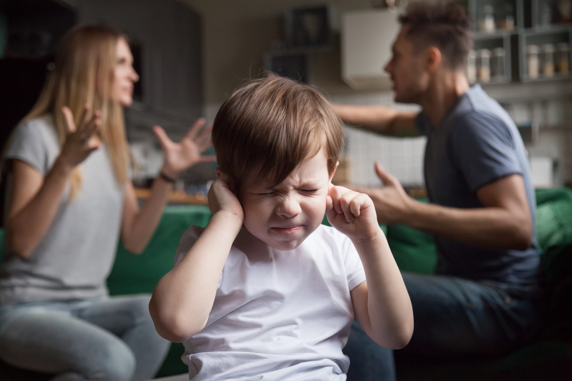 un enfant qui se bouche les oreilles car ses parents se disputent derriere lui